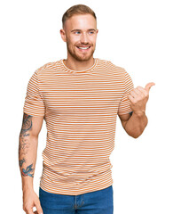 Wall Mural - Young irish man wearing casual clothes smiling with happy face looking and pointing to the side with thumb up.