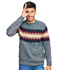 Wall Mural - Young handsome man wearing casual winter sweater doing ok gesture with hand smiling, eye looking through fingers with happy face.