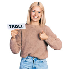 Poster - Beautiful young blonde woman holding troll banner smiling happy and positive, thumb up doing excellent and approval sign