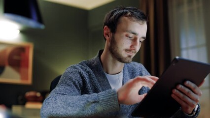Male sitting at home office. Man holding digital tablet. Male working as designer. Man freelancing at home. Male working online from home. Man relaxing at home using tablet.