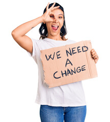 Sticker - Young woman holding we need a change banner smiling happy doing ok sign with hand on eye looking through fingers