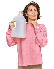 Sticker - Young hispanic woman doing laundry holding detergent bottle serious face thinking about question with hand on chin, thoughtful about confusing idea