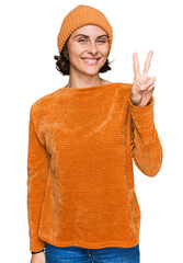 Wall Mural - Young hispanic woman wearing casual clothes and wool cap showing and pointing up with fingers number two while smiling confident and happy.