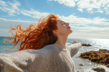 Wall Mural - Happy redhead woman with open arms and closed eyes on a rocky beach. Concept of freedom