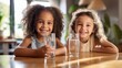 Family hydration: Kids' healthy lifestyle habit, dehydration prevention concept. Two multiracial little girls sitting at the kitchen table, feeling thirsty, drinking pure water.