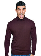 Wall Mural - Handsome hispanic man wearing casual turtleneck sweater sticking tongue out happy with funny expression. emotion concept.