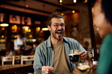 Young man laughing and having fun while drinking beer with girlfriend in pub.