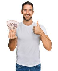 Sticker - Handsome man with beard holding 50 mexican pesos banknotes smiling happy and positive, thumb up doing excellent and approval sign