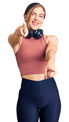 Wall Mural - Beautiful caucasian young woman wearing gym clothes and using headphones pointing to you and the camera with fingers, smiling positive and cheerful