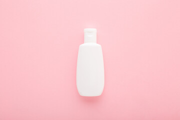 Wall Mural - White plastic cream bottle on light pink table background. Pastel color. Care about face, hands, legs and body skin. Closeup. Top down view. Empty place for text or logo.