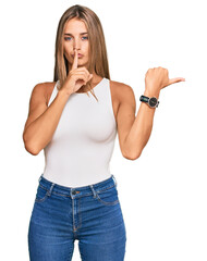 Wall Mural - Young blonde woman wearing casual style with sleeveless shirt asking to be quiet with finger on lips pointing with hand to the side. silence and secret concept.