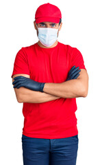 Wall Mural - Young hispanic man wearing covid-19 safety mask skeptic and nervous, disapproving expression on face with crossed arms. negative person.