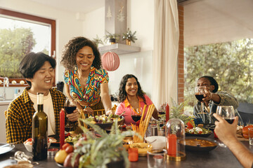 Wall Mural - Happy friends enjoying in conversation and drinking wine during festive dinner at home party