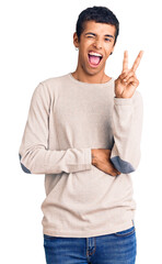 Sticker - Young african amercian man wearing casual clothes smiling with happy face winking at the camera doing victory sign. number two.