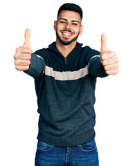 Wall Mural - Young hispanic man with beard wearing casual winter sweater approving doing positive gesture with hand, thumbs up smiling and happy for success. winner gesture.