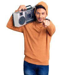 Wall Mural - Handsome latin american young man holding boombox, listening to music pointing to you and the camera with fingers, smiling positive and cheerful