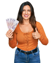 Canvas Print - Beautiful hispanic woman holding russian 500 ruble banknotes smiling happy and positive, thumb up doing excellent and approval sign