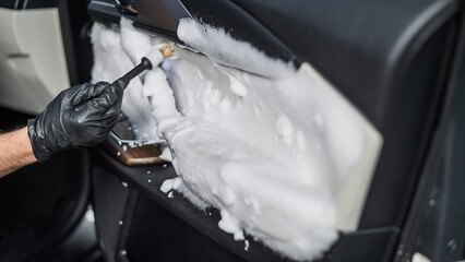 A man cleans the interior of a car with foam and a brush. Clean the door trim.