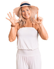 Wall Mural - Middle age fit blonde woman wearing summer hat showing and pointing up with fingers number seven while smiling confident and happy.