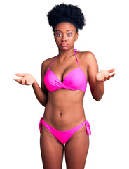 Canvas Print - Young african american woman wearing bikini clueless and confused expression with arms and hands raised. doubt concept.