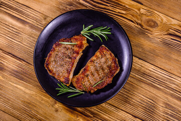 Wall Mural - Plate with roasted steaks and rosemary twigs on a wooden table. Top view