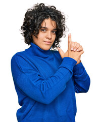 Canvas Print - Young hispanic woman with curly hair wearing turtleneck sweater holding symbolic gun with hand gesture, playing killing shooting weapons, angry face