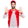 © Krakenimages.com - Young man with beard wearing baseball uniform showing and pointing up with fingers number ten while smiling confident and happy.