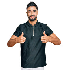 Poster - Young man with beard wearing sportswear success sign doing positive gesture with hand, thumbs up smiling and happy. cheerful expression and winner gesture.