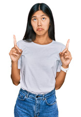 Sticker - Beautiful young asian woman wearing casual white t shirt pointing up looking sad and upset, indicating direction with fingers, unhappy and depressed.