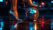 Woman feet in shiny luxury stilettos heels step on a silver sparkling disco ball on dark ball stage background with copy space, concept of party queen.