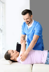 Canvas Print - Male physiotherapist working with young woman on couch in rehabilitation center