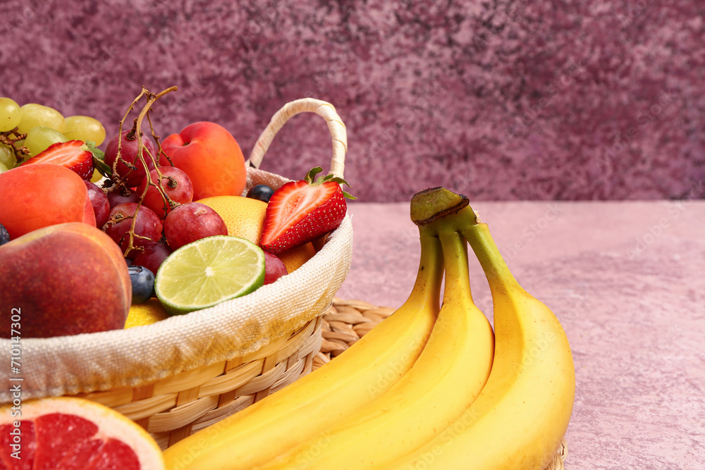 Wicker basket with different fresh fruits on pink table, closeup