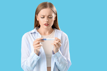 Wall Mural - Worried young woman with pregnancy test on blue background