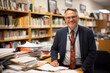 A seasoned school administrator, with a warm smile and wise eyes, sitting in his office filled with books, awards, and mementos from years of dedicated service to education