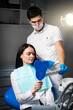 © Anton - A woman at the dentist dental chair looks at his teeth selects the color from the teeth palette
