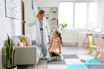 Wall Mural - Mature speech therapist teaching little girl how to pronounce letters in office