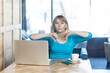 © khosrork - Portrait of serious attractive young woman with blonde hair in blue shirt working on laptop, showing thumbs down, negative feedback. Indoor shot in cafe with big window on background.