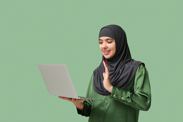 Sticker - Beautiful young Muslim woman in hijab with modern laptop on green background