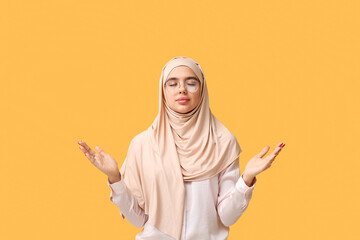 Sticker - Beautiful young Muslim woman in hijab and eyeglasses praying on yellow background