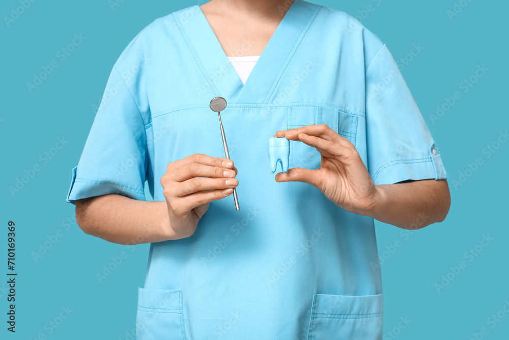 Female dentist with dental mirror and tooth model on blue background