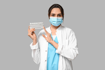 Wall Mural - Young female dentist in mask with dental shade guide on grey background