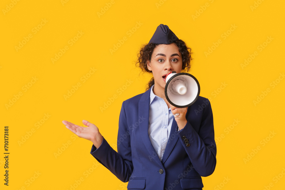 Beautiful African-American stewardess with megaphone on yellow background