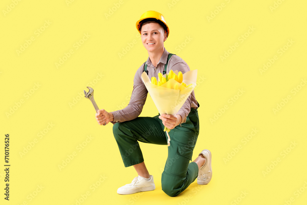 Male builder with tulips and wrench on yellow background. International Women's Day celebration