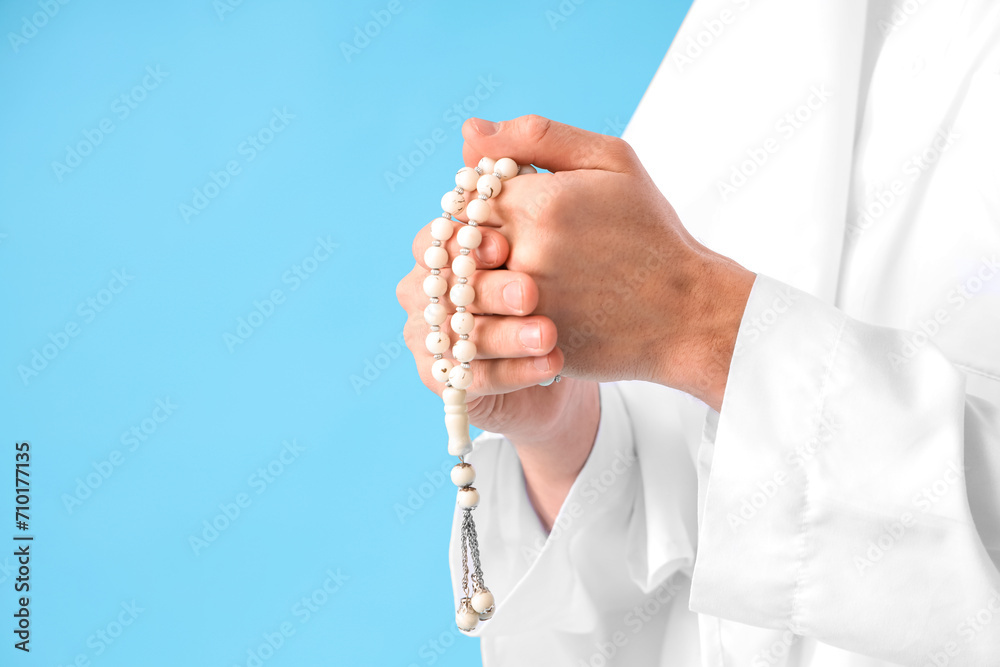 Young Muslim man with praying beads on blue background, closeup. Ramadan celebration