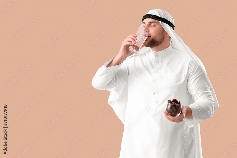 Young Muslim man with dates drinking water on beige background. Ramadan celebration