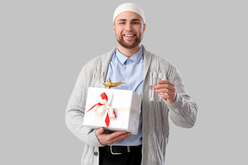 Wall Mural - Young Muslim man with glass of water and gift on light background. Ramadan celebration