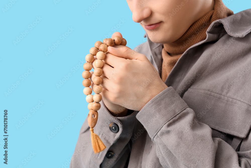 Young Muslim man with praying beads on blue background, closeup. Ramadan celebration