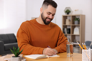 Canvas Print - Young man writing in notebook at wooden table indoors