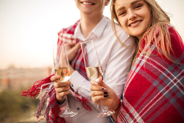 Beautiful loving couple wrapped in one blanket holding glasses of champagne smiling at camera