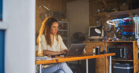 Fototapete - Hispanic Female Programmer Writing Code On Laptop Computer In Garage At Home. Woman Working On Innovative Software As A Service Startup For Business. Digital Entrepreneur Starting Company Concept.